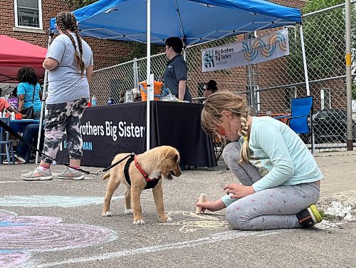 Eight year old Ari Sundell creates a drawing with chalk that was provided by the Art Gallery of Southwestern Manitoba while her Jack Russell puppy named Cosmo looks on during Saturday's “Kickin off Summer” downtown Brandon block party, a collaboration between The Dock on Princess, Section 6 Brewing Co., Kickin’ Axe., and Brandon Downtown BIZ. (Michele McDougall/The Brandon Sun) 