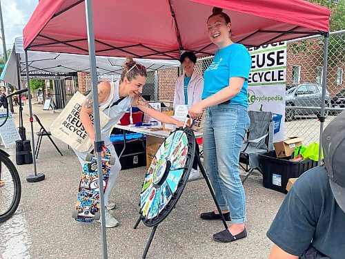 Andrea Dillan spins the wheel of recycling while Ingrid Gatin with the City of Brandon’s environmental initiatives team shares as laugh during Saturday's “Kickin off Summer” downtown Brandon block party, a collaboration between The Dock on Princess, Section 6 Brewing Co., Kickin’ Axe., and Brandon Downtown BIZ. (Michele McDougall/The Brandon Sun) 

