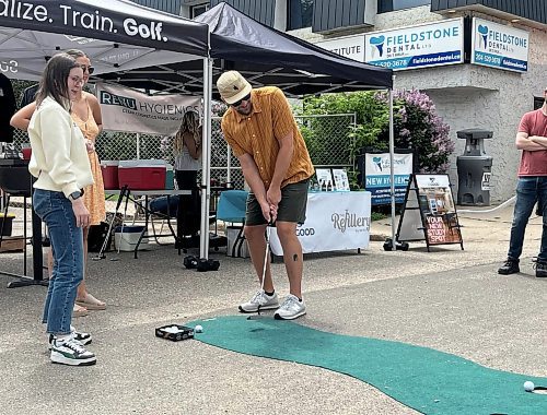 A participant tries to sink a golf ball at the putting challenge booth during Saturday's “Kickin off Summer” downtown Brandon block party, a collaboration between The Dock on Princess, Section 6 Brewing Co., Kickin’ Axe., and Brandon Downtown BIZ. (Michele McDougall/The Brandon Sun) 
 