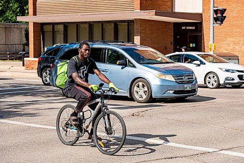 NIC ADAM / FREE PRESS
A cyclist rides past parked cars on St. Mary Ave., near Donald St., Wednesday.
240717 - Wednesday, July 17, 2024.

Reporter: Joyanne