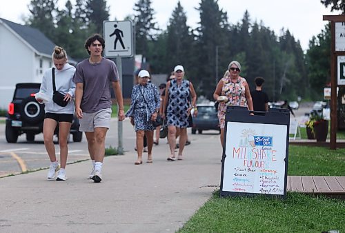 Pedestrians at Wasagaming in Riding Mountain National Park walk by a sign advertising milkshake flavours for Velvet Dip Lakeside on a warm but overcast Tuesday afternoon. (Matt Goerzen/The Brandon Sun)