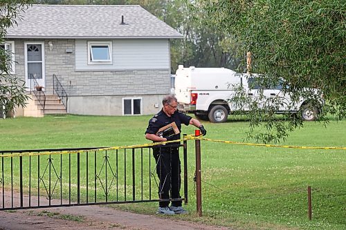 An RCMP officer adjusts the yellow tape Friday outside the rural home southeast of McCreary where police found the bodies of two men and a woman earlier in the day. (Tim Smith/The Brandon Sun)