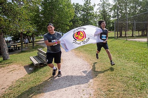 BROOK JONES / FREE PRESS
Fifteen-year-old Phoenix Abraham (left) and 17-year-old Brad Courchene carry a Sagkeeng First Nation flag as they run down the home stretch towards the finish line while competing in the Free Spirit Sprint Triathlon in Pinawa, Man., Sunday, Aug. 11, 2024.