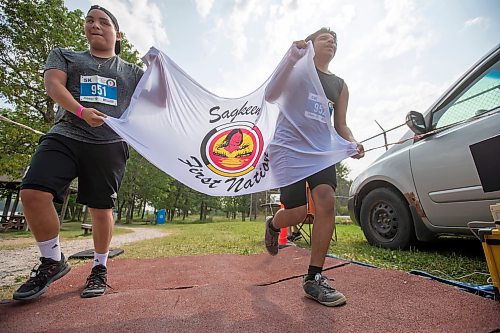 BROOK JONES / FREE PRESS
Fifteen-year-old Phoenix Abraham (left) and 17-year-old Brad Courchene carry a Sagkeeng First Nation flag as they cross the finish line after competing in the Free Spirit Sprint Triathlon in Pinawa, Man., Sunday, Aug. 11, 2024.