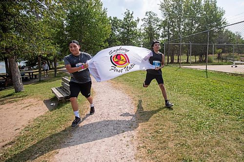 BROOK JONES / FREE PRESS
Fifteen-year-old Phoenix Abraham (left) and 17-year-old Brad Courchene carry a Sagkeeng First Nation flag as they run down the home stretch towards the finish line while competing in the Free Spirit Sprint Triathlon in Pinawa, Man., Sunday, Aug. 11, 2024.