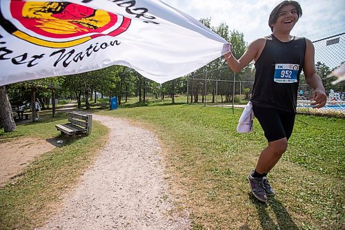 BROOK JONES / FREE PRESS
Seventeen-year-old Brad Courchene carries a Sagkeeng First Nation flag as he runs down the home stretch towards the finish line while competing in the Free Spirit Sprint Triathlon in Pinawa, Man., Sunday, Aug. 11, 2024.