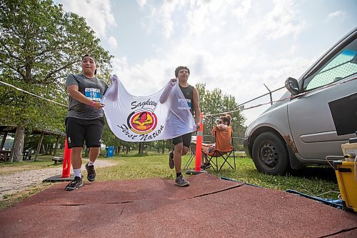 BROOK JONES / FREE PRESS
Fifteen-year-old Phoenix Abraham (left) and 17-year-old Brad Courchene carry a Sagkeeng First Nation flag as they cross the finish line after competing in the Free Spirit Sprint Triathlon in Pinawa, Man., Sunday, Aug. 11, 2024.