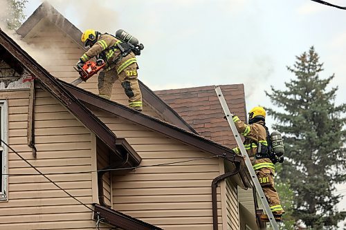 FIrefighters climb onto the roof of a burning home on First Street on Sunday afternoon to cut a hole in the roof with a chainsaw and axe. (Photos by Colin Slark/The Brandon Sun)