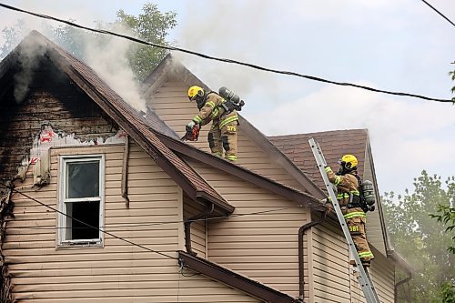 FIrefighters climb onto the roof of a burning home on First Street on Sunday afternoon to cut a hole in the roof with a chainsaw and axe. (Photos by Colin Slark/The Brandon Sun)