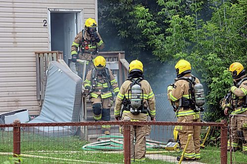 Firefighters wearing breathing apparatuses emerge from a burning home on First Street on Sunday afternoon. (Colin Slark/The Brandon Sun)