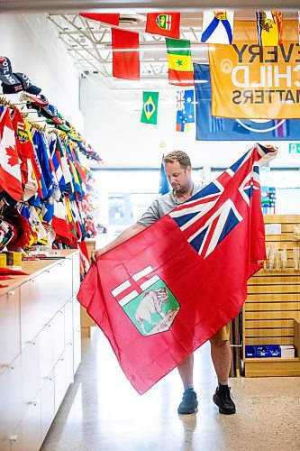 MIKAELA MACKENZIE / WINNIPEG FREE PRESS
	
Mathew Hobson, a sales associate at The Flag Shop on Osborne, shows the current Manitoba flag on Monday, Aug. 19, 2024. According to a Probe Research poll, 49% of Manitobans would support creating a new flag for the province.

Winnipeg Free Press 2024