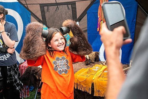 MIKAELA MACKENZIE / WINNIPEG FREE PRESS
	
Breezie Clemons (eight) has fun with the trapping tent furs as her grandpa, Dennis Duguid, takes a photo at the 6th annual Manitoba Mtis Federation elders and youth gathering at Selkirk Park on Tuesday, Aug. 27, 2024. The gathering brings together elders and youth from across the regions so that the youth can learn traditional skills, hear oral teachings and learn the principles of culturally-focused interactions with knowledge keepers.

Standup.
Winnipeg Free Press 2024