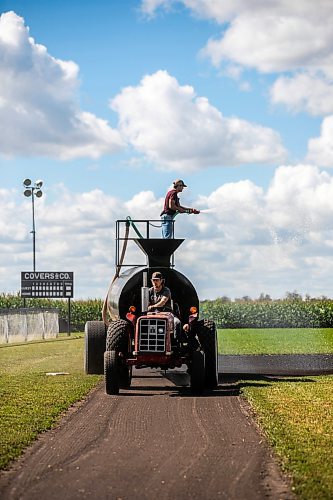 Joe Gardiner drives the tractor as Jace Guilford waters the infield at the Field of Dreams baseball diamond near Clearwater, Manitoba on Thursday. (Mikaela MacKenzie/Winnipeg Free Press)