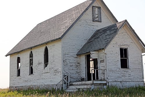 The Berbank Memorial Church has fallen into disrepair. The windows are shattered and material once installed to protect them has ripped off. A piece of the front door hangs on rusty hinges, and many shingles from the roof lay in the nearby grass overgrowing the steps. (Connor McDowell/Brandon Sun)