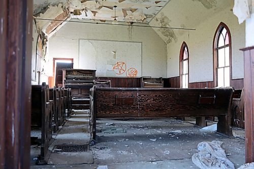 The floor of the Berbank Memorial Church is covered with scraps. Graffiti is painted at the front, the back door lays broken and leaning inwards against a piano, and material on the ceiling is peeling. (Connor McDowell/Brandon Sun)