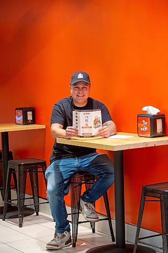 BROOK JONES / FREE PRESS
Thirty-year-old Eric Saniuk who is the owner of Blazing Chicken Shack is pictured sitting at a table as he holds a menu at his restaurant at 392 Graham Ave., in Winnipeg, Man., Monday, Sept. 16, 2024. Saniuk hosted a grand opening Friday, Sept. 13, 2024.