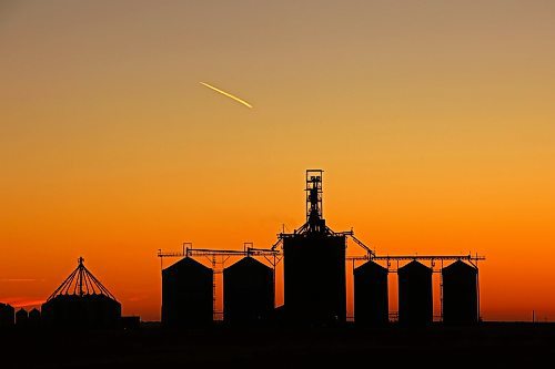 An airplane leaves a contrail across the orange sky over the Richardson Pioneer grain terminal in Kemnay shortly before sunrise. (Tim Smith/The Brandon Sun) 