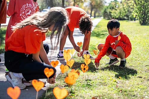 MIKAELA MACKENZIE / FREE PRESS
	
Students Dasha (left, grade eight), Xavier (centre, grade seven), and Marius (right, grade two) place orange hearts along the walkway project at cole Van Walleghem School Thursday, Sept. 26, 2024. 

For Maggie story.
Winnipeg Free Press 2024