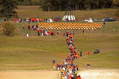 Participants make their way from Grand Valley Road across a field to the former Brandon Residential School site during the Truth and Reconciliation Week 2024 Orange Shirt Day Walk on Monday. The walk began and ended at the Riverbank Discovery Centre grounds with speeches, teaching and ceremony at the former residential school site. Orange hearts line the hill at the site in memory of children who died while attending the school. (Tim Smith/The Brandon Sun)