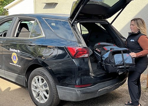 Niki Harper with Vision Loss Rehabilitation Canada, a sister organization to CNIB, loads a tote bag into the back of a 2024 black Chevrolet Equinox that was purchased by the Wheat City Lions Club and donated to the two non-profits. (Michele McDougall/The Brandon Sun)