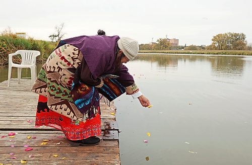 Julia Brandon places flower petals in the Assiniboine River in memory of her sister Victoria Brandon. (Tim Smith/The Brandon Sun)