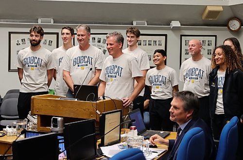 Grant Hamilton, Brandon University's director of marketing and communications is surrounded by members of the men and women's volleyball teams in Brandon Council Chambers Monday evening. Hamilton requested permission to to paint the bobcat logo in the t-intersection of Louise Avenue and 20th Street in front of Brandon University's Healthy Living Centre to promote the 2025 U Sports Men's Volleyball National Championship in March of 2025. (Michele McDougall/The Brandon Sun) 