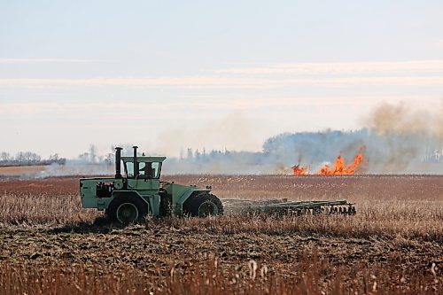 A farmer cultivates his field outside of Souris on Saturday afternoon while a stubble fire burns in the background. (Connor McDowell/Brandon Sun)