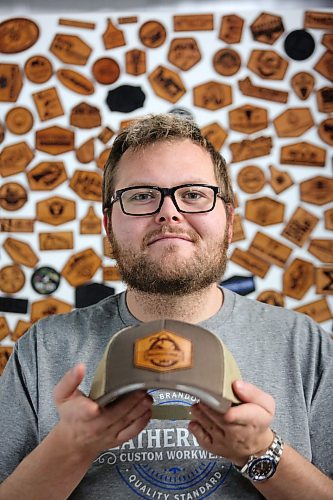 Leatherwood Custom Workwear owner Morgan James holds one of his company's products while sitting in front of his leather logo wall on Monday. James says the ongoing Canada Post strike has caused considerable trouble for his Brandon-based company, as nearly all of his business is conducted through the mail. (Matt Goerzen/The Brandon Sun)