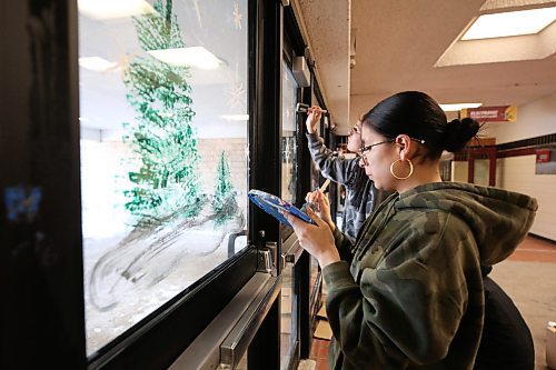 Grade 11 student Harmonee Moar-Sanderson dabs at her paint palette while painting stars on a front door window at Crocus Plains Regional Secondary School on Friday morning, part of an art project with instructor Anne Boychuk to paint a holiday theme on the high school's front entrance. (Matt Goerzen/The Brandon Sun)