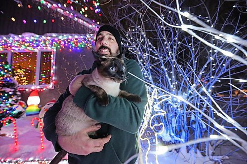 Brandon resident Patrick Stewart holds his family cat Avi, a seven-month-old Siamese feline, outside their brightly-lit home at 522 22nd Street on Monday evening. Stewart and his family have worked since November to set up all the lights used in the holiday display, as a means to raise funds for One At A Time Rescue, a Brandon-based organization that focuses primarily on orphaned animals. (Matt Goerzen/The Brandon Sun)