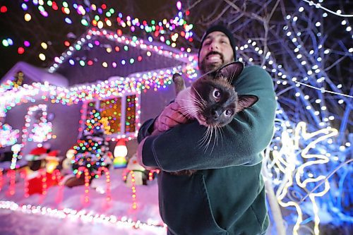 Brandon resident Patrick Stewart holds his family cat Avi, a seven-month-old Siamese feline, outside their brightly-lit home at 522 22nd Street on Monday evening. Stewart and his family have worked since November to set up all the lights used in the holiday display, as a means to raise funds for One At A Time Rescue, a Brandon-based organization that focuses primarily on orphaned animals. (Matt Goerzen/The Brandon Sun)