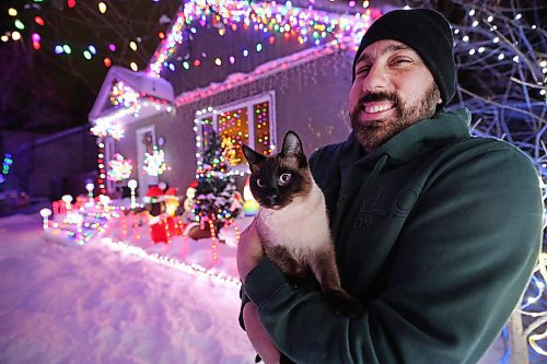 Brandon resident Patrick Stewart holds his family cat Avi, a seven-month-old Siamese feline, outside their brightly-lit home at 522 22nd Street on Monday evening. Stewart and his family have worked since November to set up all the lights used in the holiday display, as a means to raise funds for One At A Time Rescue, a Brandon-based organization that focuses primarily on orphaned animals. (Matt Goerzen/The Brandon Sun)