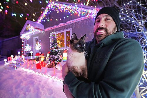 Brandon resident Patrick Stewart holds his family cat Avi, a seven-month-old Siamese feline, outside their brightly-lit home at 522 22nd Street on Monday evening. Stewart and his family have worked since November to set up all the lights used in the holiday display, as a means to raise funds for One At A Time Rescue, a Brandon-based organization that focuses primarily on orphaned animals. (Matt Goerzen/The Brandon Sun)