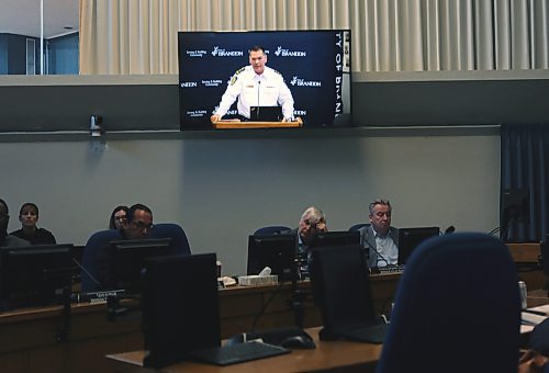 While speaking from the podium at City Hall, Brandon Police chief Tyler Bates is projected on a television screen above members of the police board on Friday. Bates told the police board on Friday that police want to grow their footprint in the downtown core this summer. (Connor McDowell/Brandon Sun)