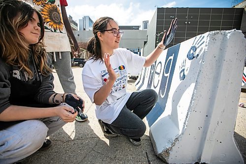 MIKAELA MACKENZIE / FREE PRESS
	

Hugh John MacDonald School grade nine students Charisma Wozny (centre) and Athena Abuda (left) paint a concrete barrier ahead of the whiteout street parties near Donald and Graham on Thursday, April 17, 2025. 

Winnipeg Free Press 2025