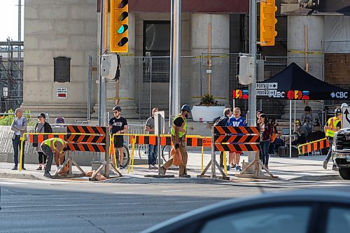 MIKE DEAL / FREE PRESS
construction crews remove the last of the barriers while impatient pedestrians cross the street at Portage Avenue and Main Street just hours before they officially open Friday morning. 
20250627 - June 27, 2025