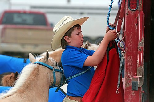 A young cowboy named Conner hooks up feed bags to the side of a trailer. (Matt Goerzen/The Brandon Sun)