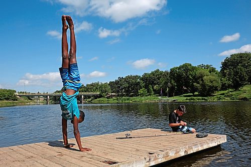 Kai Denbow walks on his hands as his friend Nathan Holden fishes from a dock along the Souris River in Souris on a hot Tuesday. (Tim Smith/The Brandon Sun)