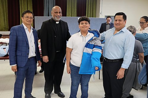 Cleo Castillo of Knights of Columbus Manitoba and St. Hedwig Catholic Church Pastor Philip Malayil join Mario Zelaya, who got a new winter coat, and his father, Mario, during the coat donation at St. Hedwig Catholic Church on Sunday afternoon. Children in the Spanish-speaking community at St. Hedwig Catholic Church received new winter coats from the Knights of Columbus Manitoba. (Abiola Odutola/The Brandon Sun)