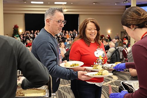 Andrea and Marc Plante prepare to serve a hot meal to people sitting at tables at the Victoria Inn for the 40th anniversary of the Westman and Area Traditional Christmas Dinner. (Tessa Adamski/The Brandon Sun)