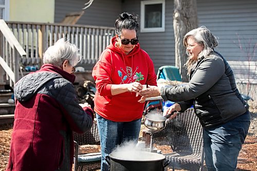 MIKAELA MACKENZIE / FREE PRESS
Louise May (right) hands cups of in-progress syrup to Naomi Gerrard (left) and Christine Cyr by the fire on Tuesday, April 21, 2026.
Standup.
Free Press 2026