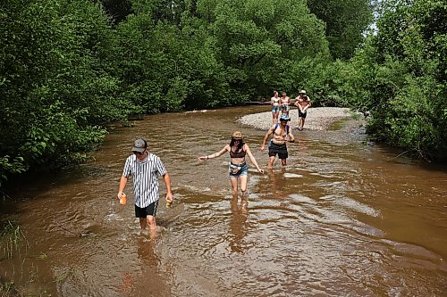 Festivalgoers wade through the creek that runs past the campground area at Dauphin’s Countryfest 2026 on Friday afternoon. (Tim Smith/The Brandon Sun)