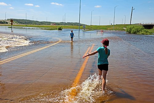 13072026
Siblings Brooks and Emily Zamrykut wade in the flood waters of the Assiniboine River pouring over Grand Valley Road near the Trans Canada Highway on a scorching hot Monday afternoon.
(Tim Smith/The Brandon Sun)