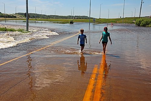 13072026
Siblings Brooks and Emily Zamrykut wade in the flood waters of the Assiniboine River pouring over Grand Valley Road near the Trans Canada Highway on a scorching hot Monday afternoon.
(Tim Smith/The Brandon Sun)