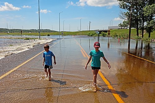 13072026
Siblings Brooks and Emily Zamrykut wade in the flood waters of the Assiniboine River pouring over Grand Valley Road near the Trans Canada Highway on a scorching hot Monday afternoon.
(Tim Smith/The Brandon Sun)