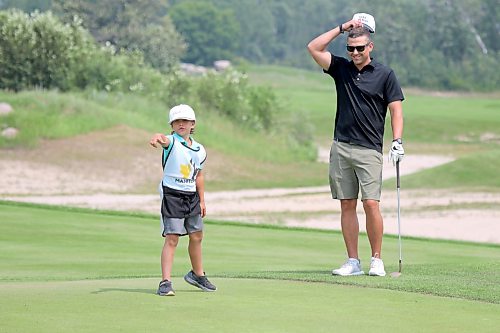 Doug Penner listens as caddy and seven-year-old son Liam reads the 15th green. (Thomas Friesen/The Brandon Sun)