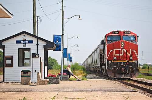 A shirtless man sits just outside the Via Rail station on a hot summer afternoon in Rivers, Man. while watching a Canadian National train pass by on Wednesday. (Matt Goerzen/The Brandon Sun)