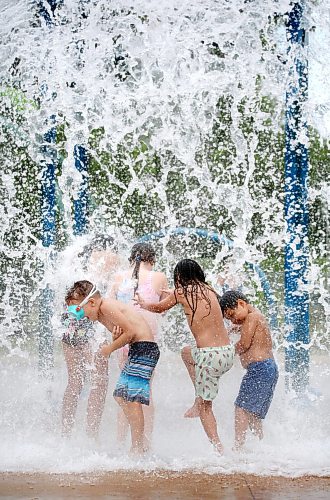 A crowd of kids get cool with a huge spray of water from the giant dump bucket at the Rideau Park Splash Pad on a pleasantly warm Friday afternoon. (Matt Goerzen/The Brandon Sun)