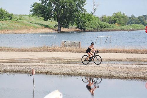 A cyclist is reflected in the flood waters off First Street North on a hot Monday afternoon in Brandon. (Matt Goerzen/The Brandon Sun)