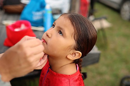 Five-year-old jingle dancer Iris Bunn of Birdtail Sioux Dakota Nation holds still as her mother, Faith Other, helps her with her lipstick prior to the grand entry. (Tim Smith/The Brandon Sun)